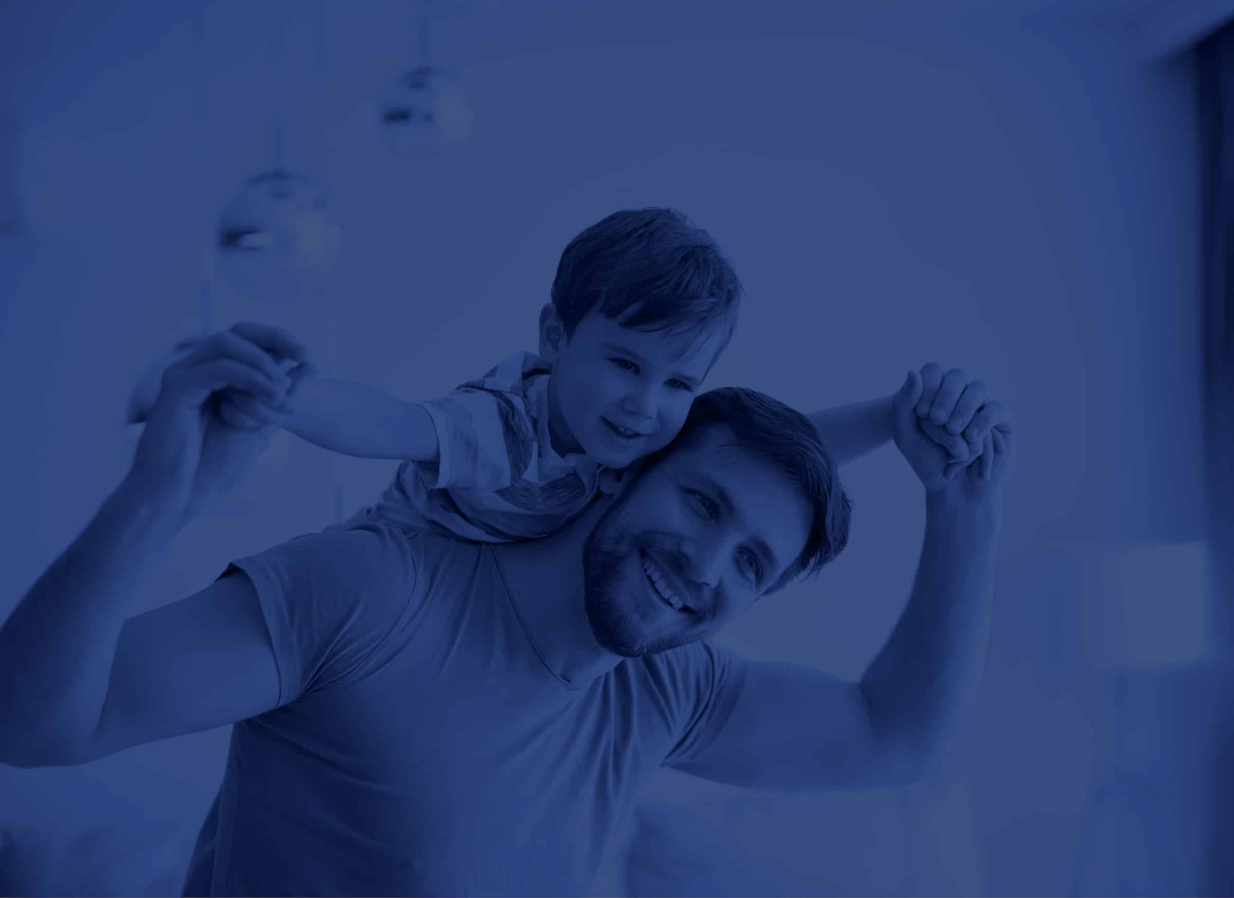 A smiling man holds a young boy on his back. They are indoors, holding hands and looking happy. The image has a blue overlay.